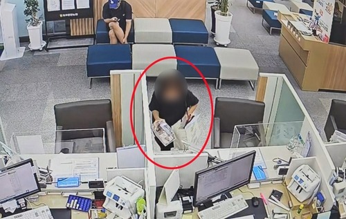 은행 창구 위에 있는 불우이웃돕기 모금함을 쇼핑백에 담고 있는 피의자. / 사진=연합뉴스